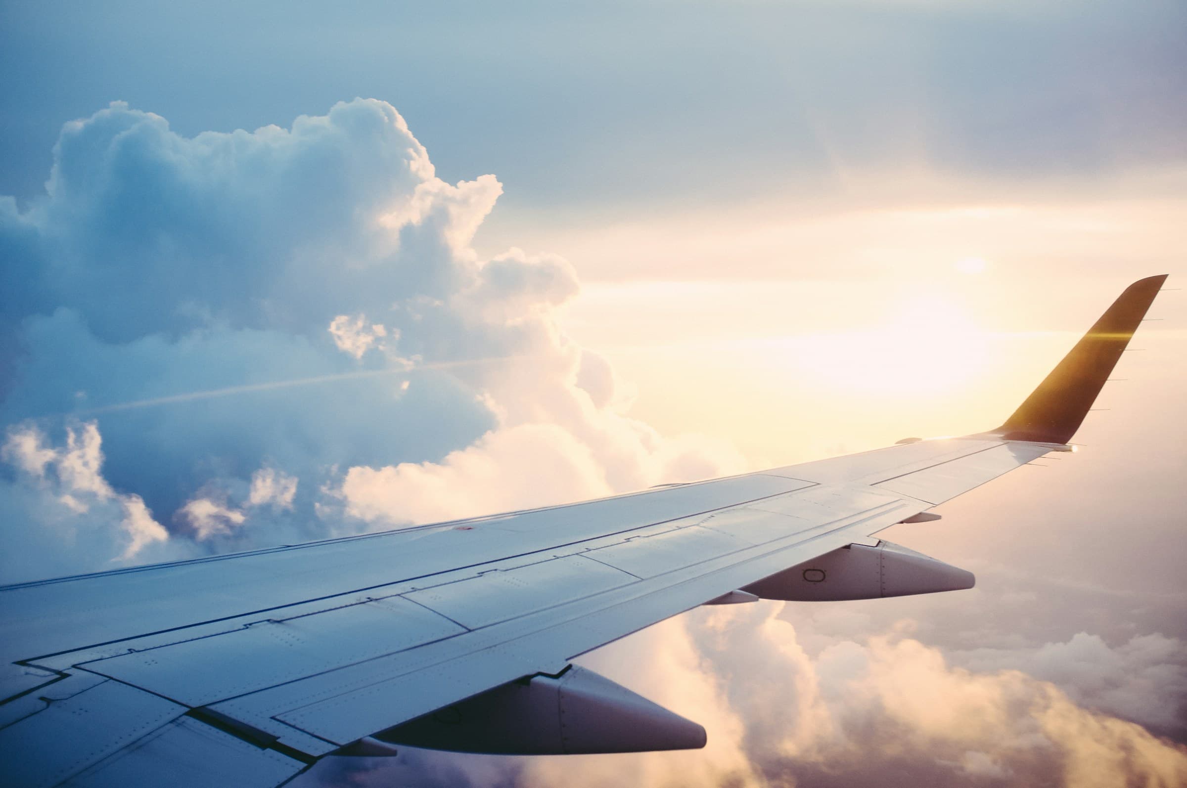 Airplane wing above clouds at sunrise for global travel deals
